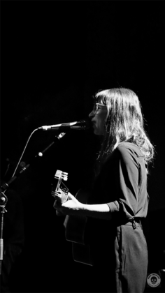 Sängerin mit Gitarre am Mikrofon. Seitlich fotografiert in schwarz weiß.