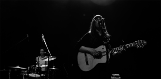 Sängerin mit Gitarre am Mikrofon. Frontal fotografiert in schwarz weiß.
